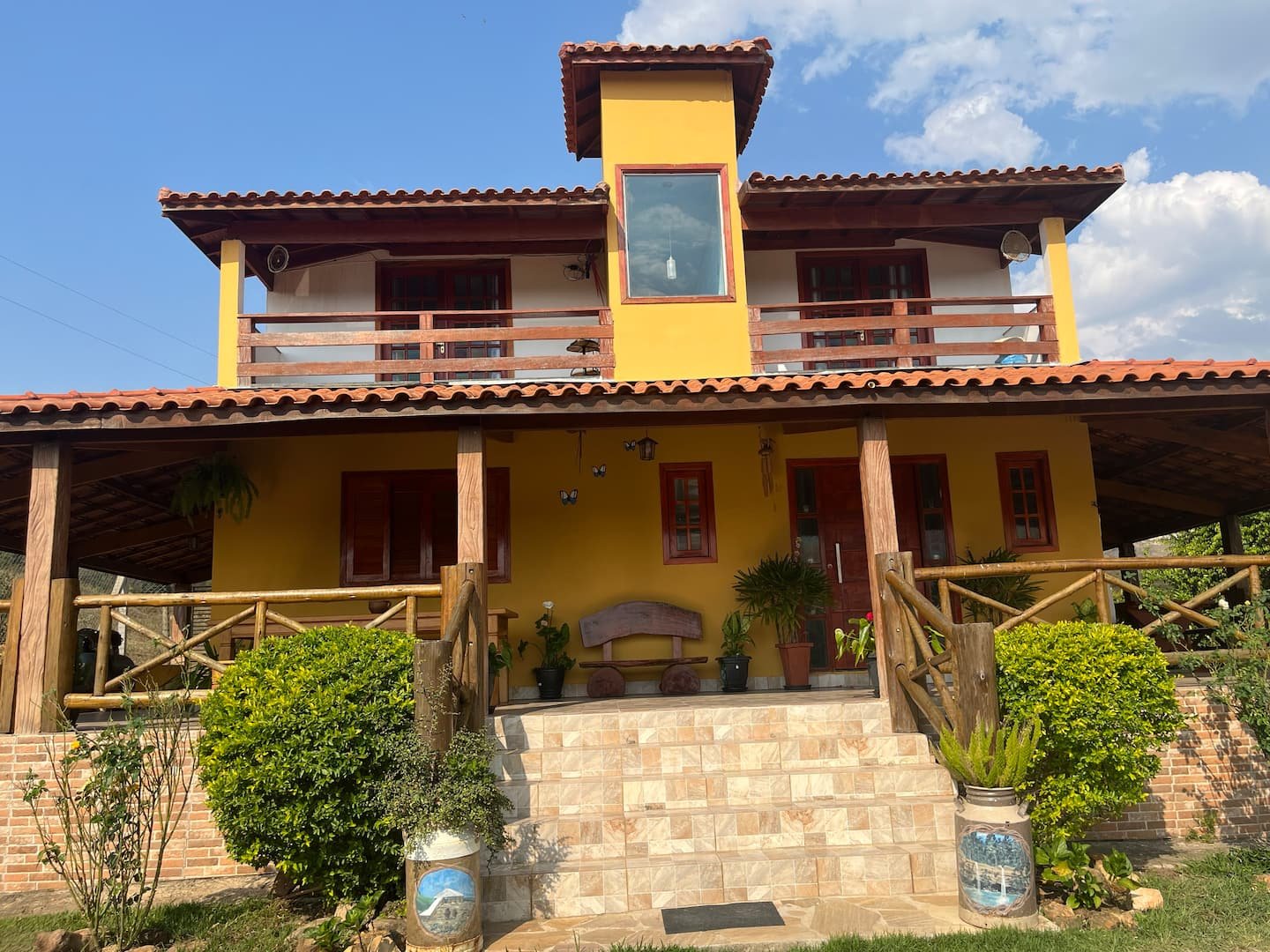 Fachada frontal da casa grande, com escada, varanda e dois pavimentos.