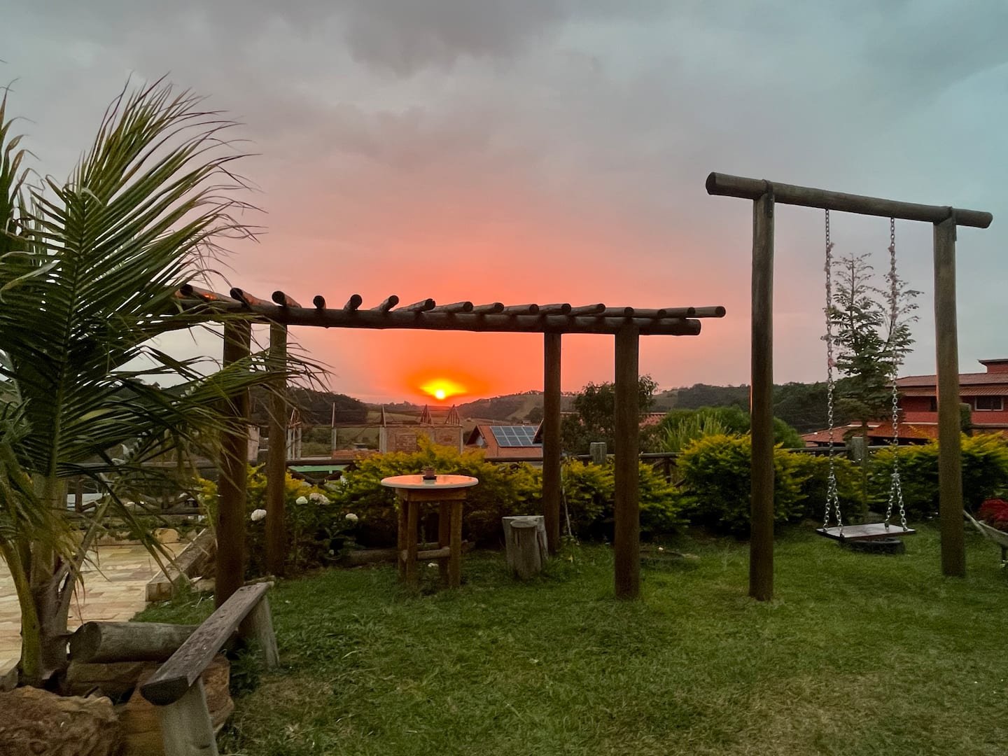Jardim com pergolado e bancos ao pôr do sol, na galeria da Casa Borboleta Azul
